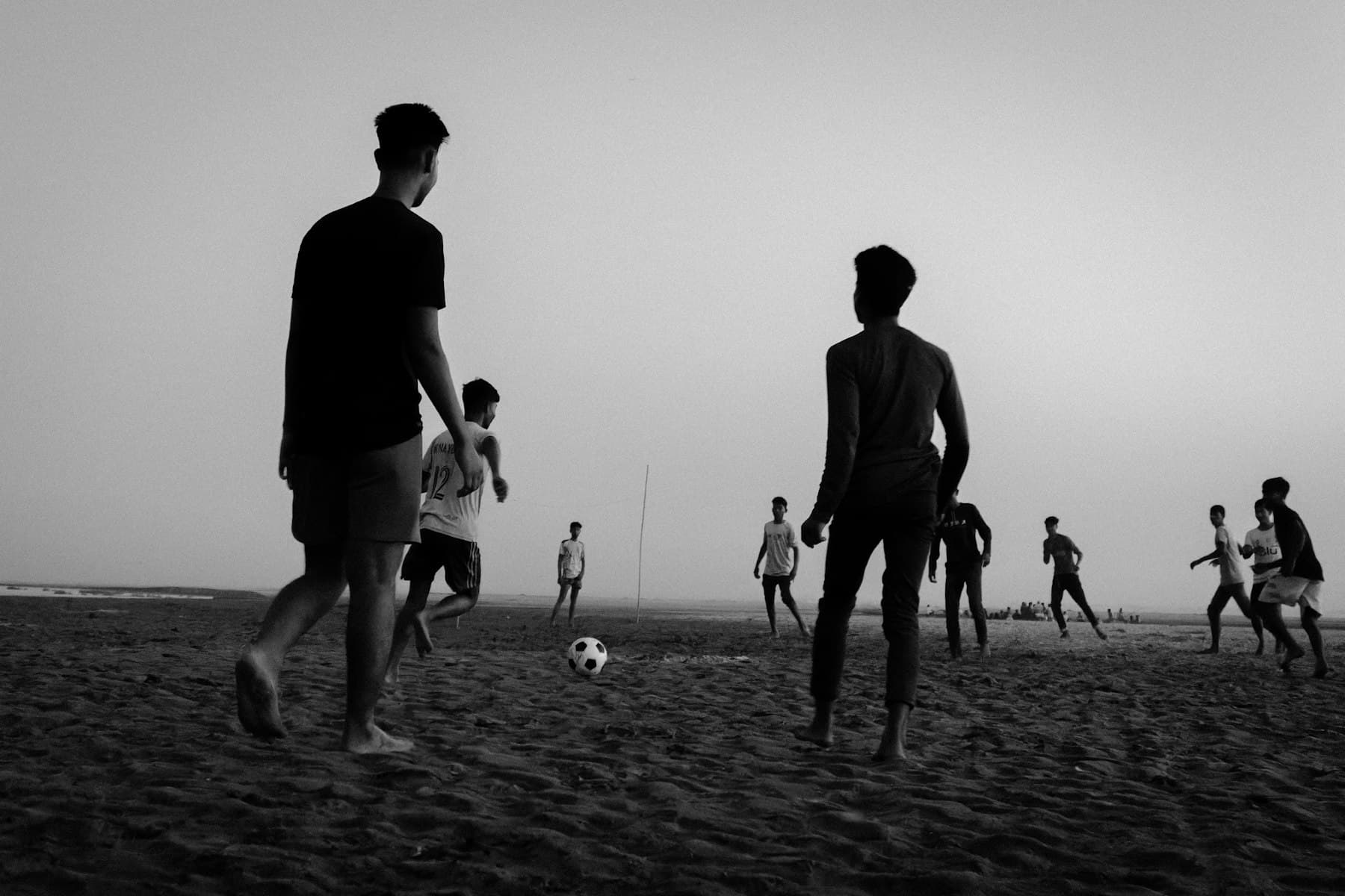 Young men playing football on an open riverbed at dusk in Bangladesh