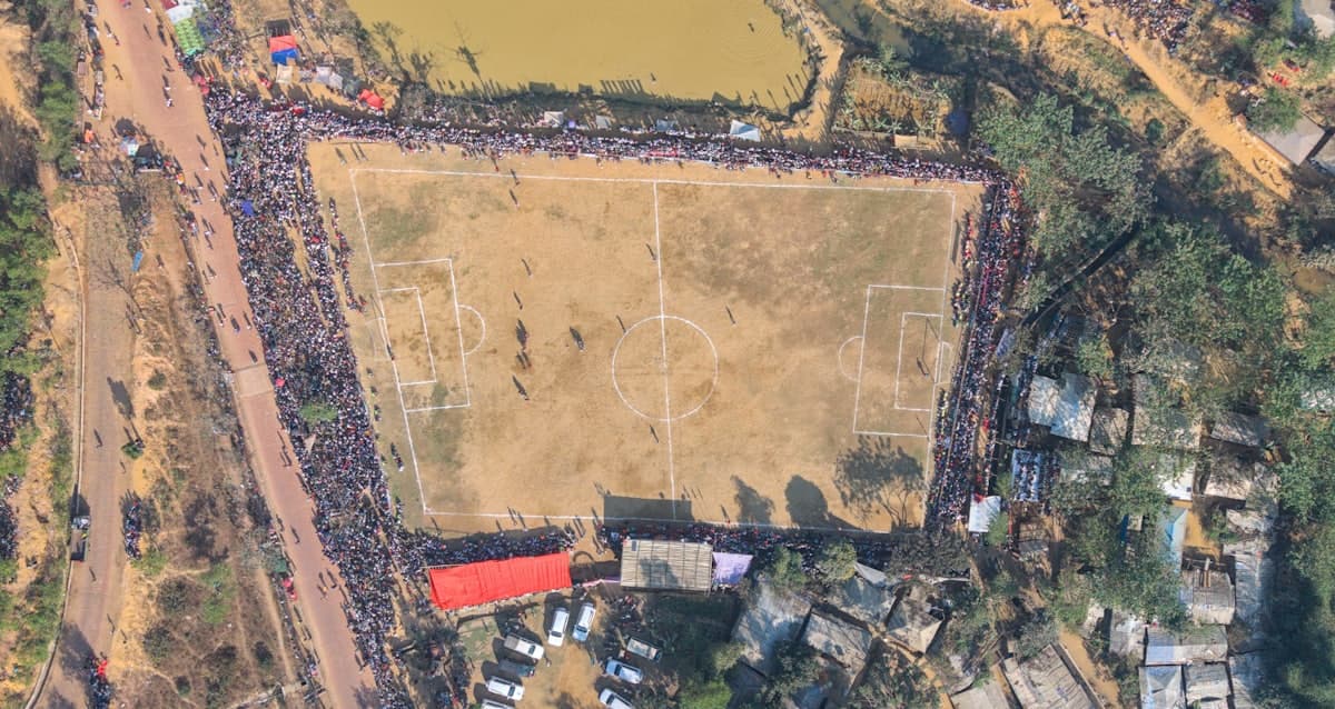 Aerial view of a packed crowd ringing a dirt pitch on matchday